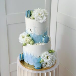 Na zdjęciu tort artystyczny w kolorach niebiesko białych, udekorowany makaronikami oraz żywymi kwiatami - wykonany w Częstochowie przez Słodkości dla gości