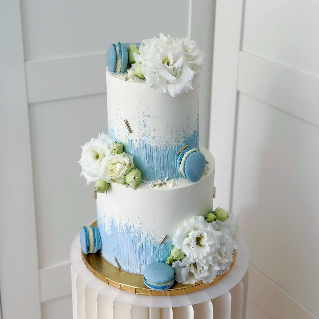 Na zdjęciu tort artystyczny w kolorach niebiesko białych, udekorowany makaronikami oraz żywymi kwiatami - wykonany w Częstochowie przez Słodkości dla gości